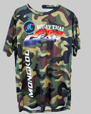 A short-sleeve camouflage t-shirt hanging on a wooden hanger against a wooden slat wall. The shirt features a green, brown, and black camo pattern with a large graphic on the chest reading 'MUAY THAI FIGHT GEAR' and 'MONGKOL' printed vertically on the left side.